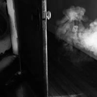 A hand drapes our from bed engulfed in smoke in black and white